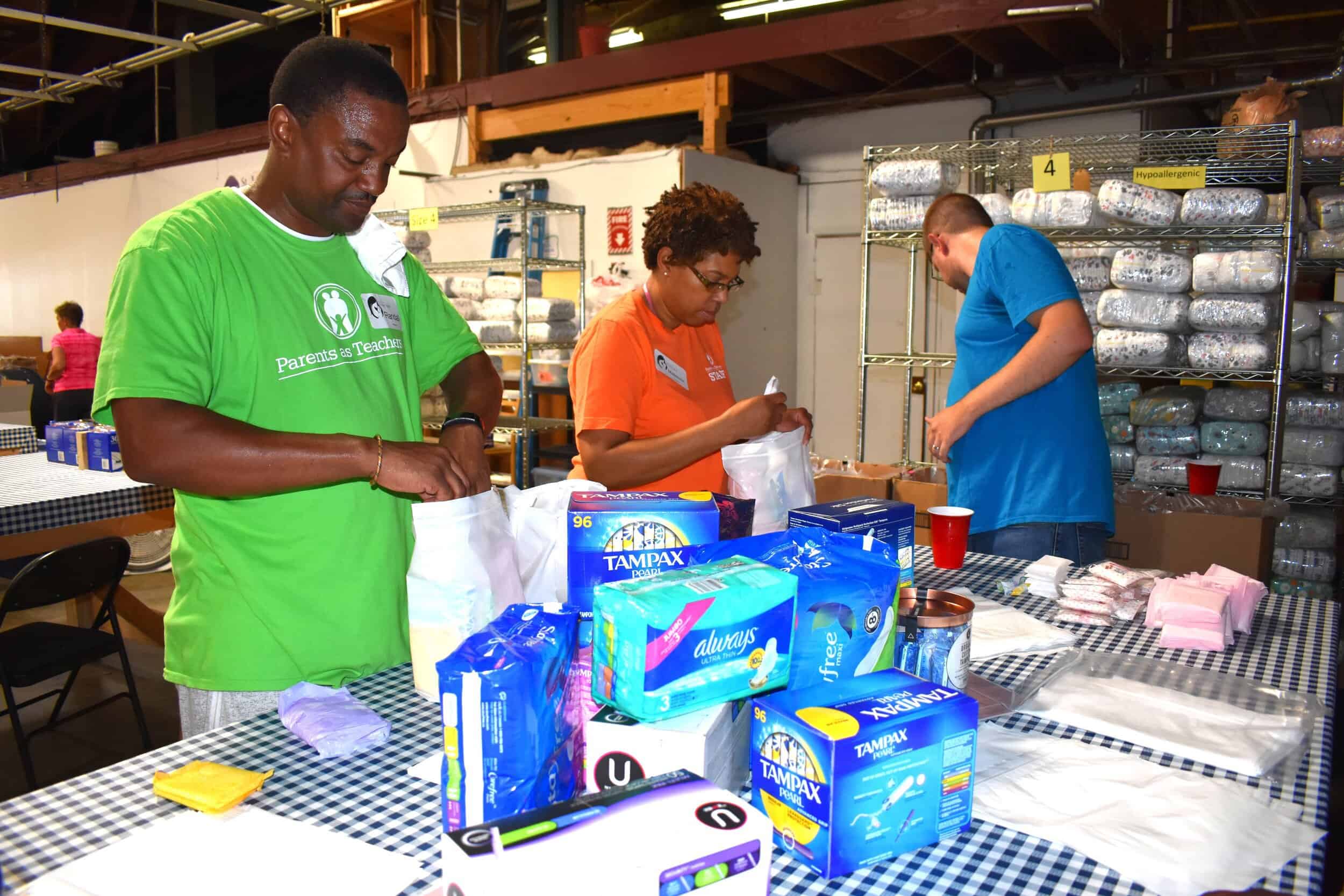 Parents as Teachers staffers Randall Hinton, Madeliene Brice, and Rick Evers prepare feminine hygiene product kits for distribution to area low-income women at the St. Louis Diaper Bank as part of PAT’s giving back to the community initiative on the…