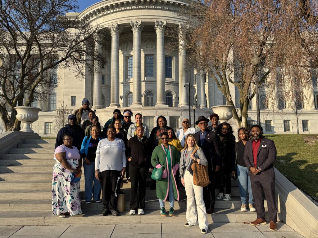 Diverse group of people posing on steps in front of a grand neoclassical building with tall columns and leafless trees