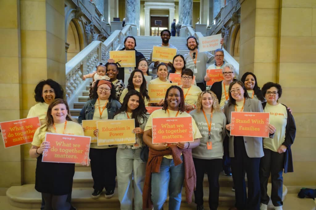 Diverse group of smiling people on marble steps holding signs reading "What we do together matters" and "Stand With Families."